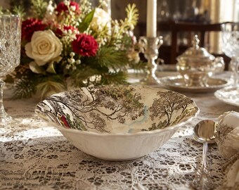 May include: A white ceramic bowl with a scalloped edge featuring a detailed transferware print of a landscape with trees and a small blue stream. The bowl has a glossy finish and is positioned on a white lace tablecloth with a floral centerpiece.