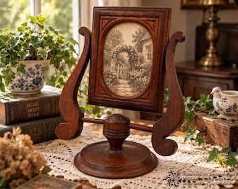 May include: A dark brown wooden swivel picture frame with a rectangular outer edge and an oval inner opening. The frame holds a sepia-toned print of a garden path with a floral archway. It is supported by a circular base and two curved side arms.