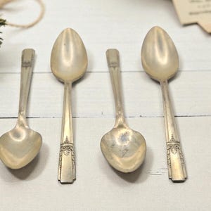 May include: Four vintage silver spoons with oval bowls and ornate handle details. The spoons are arranged on a white surface, showcasing their aged patina. The spoons are a classic addition to any antique collection.
