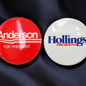 May include: Two vintage campaign buttons. One is red with the name "Anderson" in white and the text "FOR PRESIDENT". The other is white with the name "Hollings" in blue and the text "PRESIDENT".