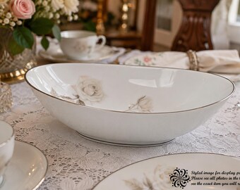 May include: A white oval porcelain serving bowl featuring a delicate grey rose floral pattern and a thin silver rim. The bowl has a smooth, glossy finish and a curved, deep basin design, presented as a piece of fine dining tableware.