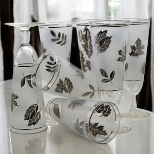 May include: Set of five frosted glass tumblers with silver leaf designs. The glasses have a silver rim and are decorated with various leaf shapes.