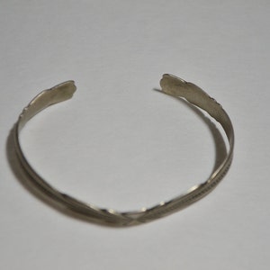 May include: A silver bracelet with a simple, elegant design. The bracelet is made of a single band of metal with a slightly curved shape.