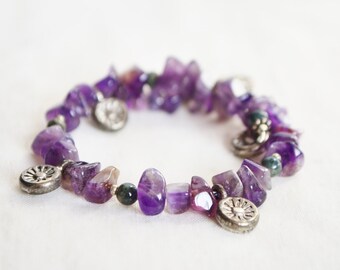 May include: A purple amethyst gemstone bracelet with silver charms. The bracelet is made of irregular shaped amethyst stones and has several silver charms with a floral design.