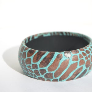 May include: A turquoise and brown patterned bangle bracelet. The bracelet is made of a hard material and has a smooth, glossy finish.