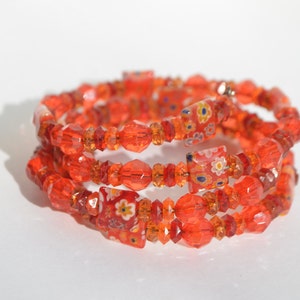 May include: A multi-strand bracelet made of orange and clear glass beads. The beads are faceted and some have a floral pattern.