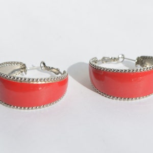 May include: A pair of red hoop earrings with a silver beaded trim. The earrings are made of metal and have a shiny finish.