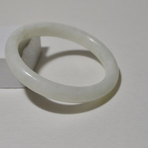May include: A white jade bangle bracelet. The bangle is smooth and polished, with a slightly oval shape.