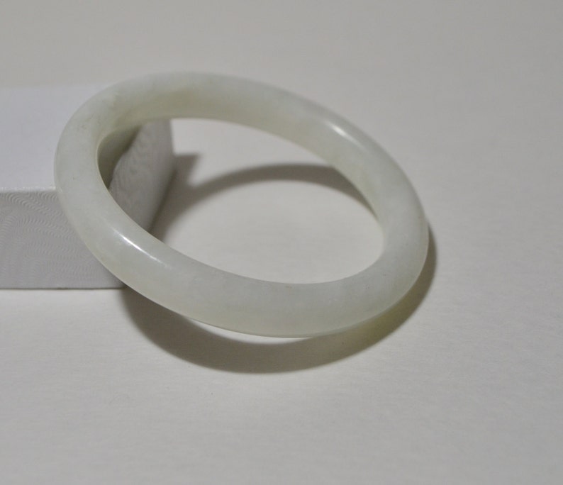 May include: A white jade bangle bracelet. The bangle is smooth and polished, with a slightly oval shape.