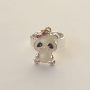May include: A silver ring with a white panda charm. The panda has pink accents and black eyes. The charm is attached to the ring with a silver loop.