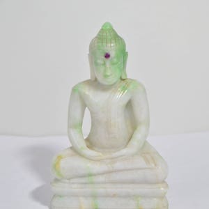 May include: A white jade Buddha statue with a green patina and a pink gemstone in the forehead. The Buddha is seated in meditation with hands in the Dhyana mudra.
