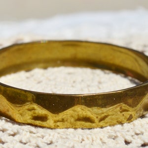May include: A gold-toned metal bangle bracelet with a faceted design. The bracelet is smooth and shiny.