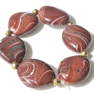 May include: A bracelet featuring seven large, oval-shaped beads. The beads are a deep reddish-brown color with swirling white and gray patterns. Small, gold-colored beads separate each of the larger beads. The bracelet is on a white background.