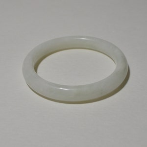 May include: A white jade bangle bracelet. The bangle is smooth and polished, with a slightly cloudy appearance.