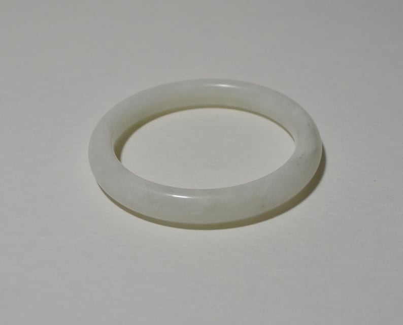 May include: A white jade bangle bracelet. The bangle is smooth and polished, with a slightly cloudy appearance.