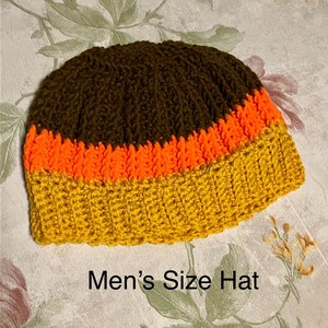 May include: A crocheted hat with brown, orange, and yellow stripes. "Men's Size Hat" is written below the hat.
