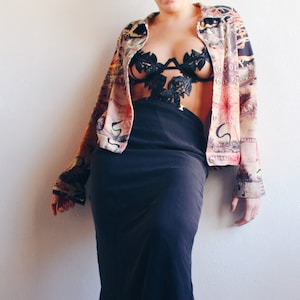 Peut inclure: Une femme portant une jupe noire et une veste à motifs avec un soutien-gorge en dentelle noire en dessous. Elle porte des bottes noires.