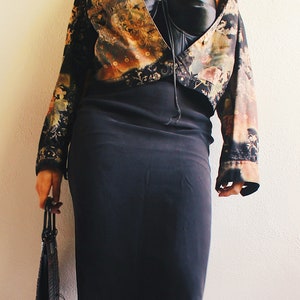 Peut inclure: Une veste courte à motif noir et or avec un haut noir sans bretelles et une jupe noire. La veste a un motif floral et la jupe est une jupe crayon.