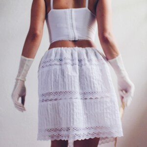 Pu&ograve; includere: Una gonna di pizzo bianco con un bordo di pizzo bianco. La gonna &egrave; plissettata e ha una vita aderente.