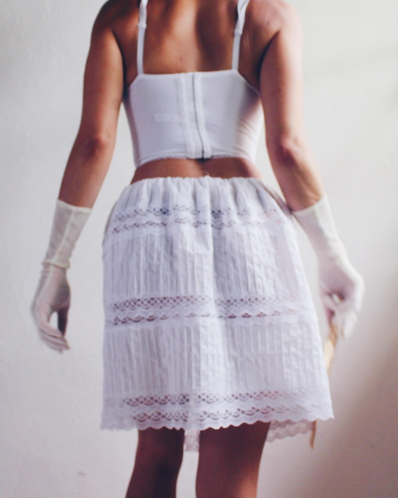 Pu&ograve; includere: Una gonna di pizzo bianco con un bordo di pizzo bianco. La gonna &egrave; plissettata e ha una vita aderente.