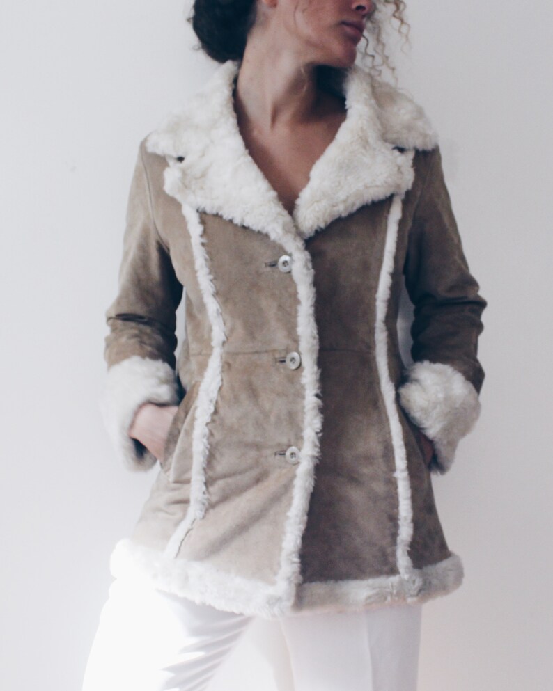 May include: A brown suede jacket with a white faux fur collar and trim. The jacket has a button closure and pockets.