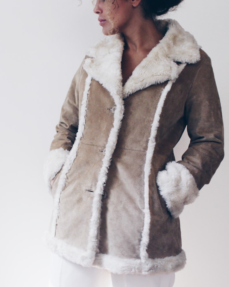 May include: A brown suede jacket with a white faux fur collar and cuffs. The jacket has a button closure and two pockets.