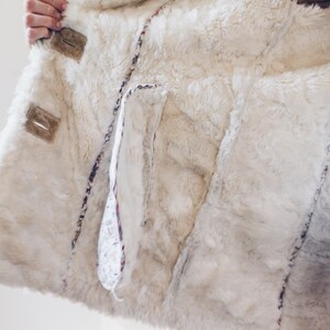 May include: A white faux fur jacket with a brown suede trim and a floral patterned lining. The jacket has a large pocket on the inside.