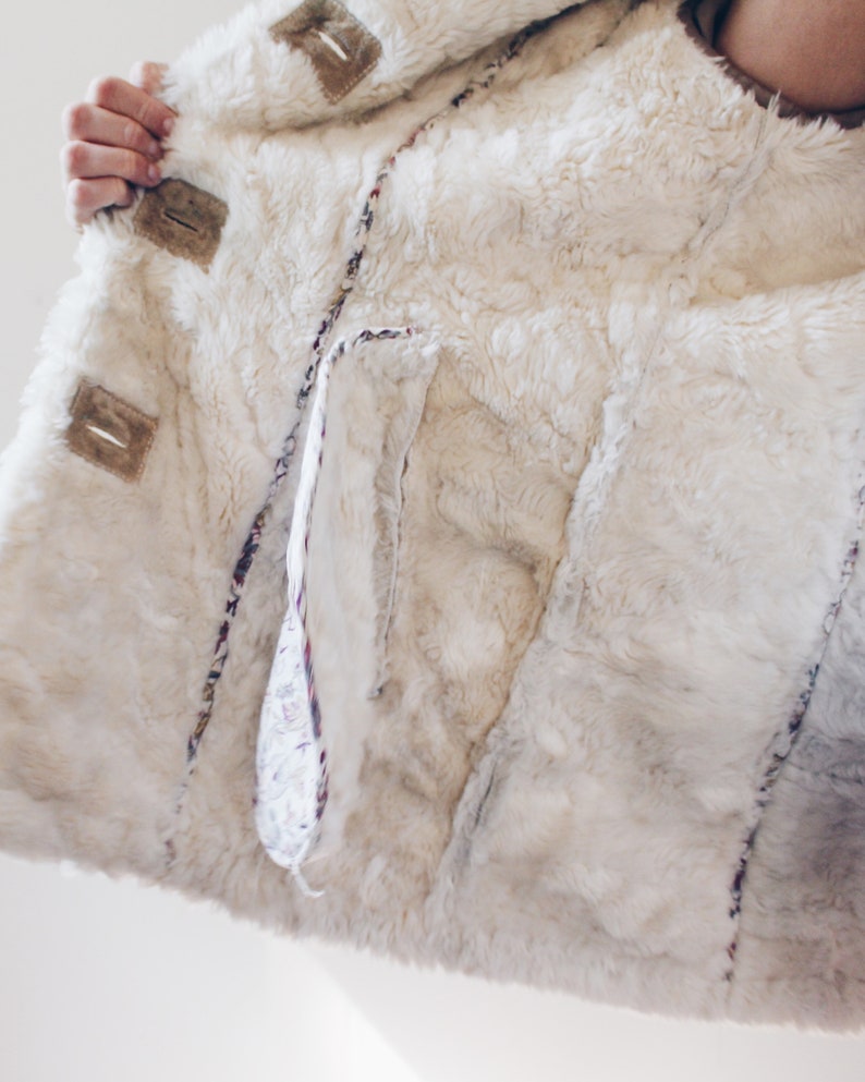 May include: A white faux fur jacket with a brown suede trim and a floral patterned lining. The jacket has a large pocket on the inside.
