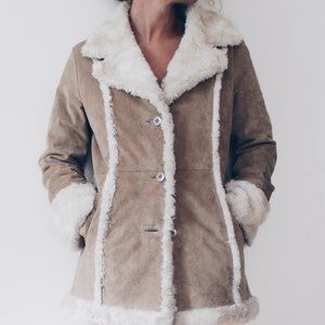 May include: A brown suede jacket with a white faux fur collar and lining. The jacket has a button closure and two pockets.