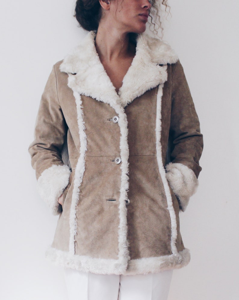May include: A brown suede jacket with a white faux fur collar and lining. The jacket has a button closure and two pockets.