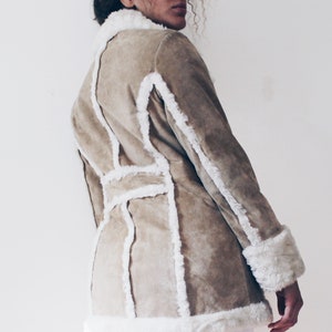 May include: A brown suede jacket with white faux fur trim. The jacket has a belted waist and long sleeves.