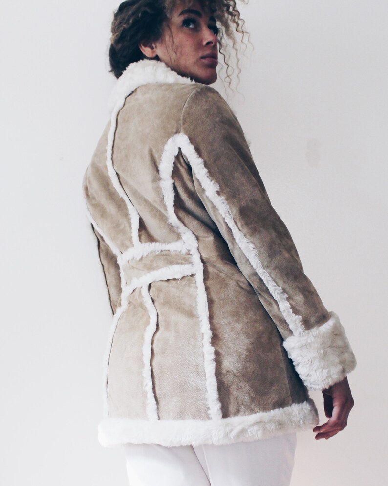 May include: A brown suede jacket with white faux fur trim. The jacket has a belted waist and long sleeves.