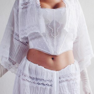 Pu&ograve; includere: Un top bianco in pizzo con un bordo in pizzo bianco e una gonna bianca in pizzo. Il top ha una scollatura a cuore e la gonna ha un vita alta.