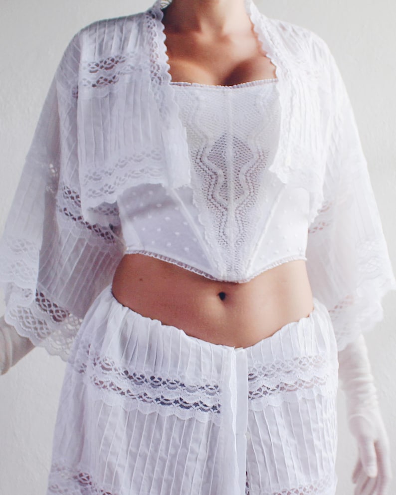 Pu&ograve; includere: Un top bianco in pizzo con un bordo in pizzo bianco e una gonna bianca in pizzo. Il top ha una scollatura a cuore e la gonna ha un vita alta.