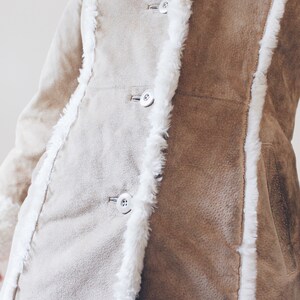 May include: A brown suede jacket with a white faux fur trim. The jacket has a button closure and a pocket on the right side.