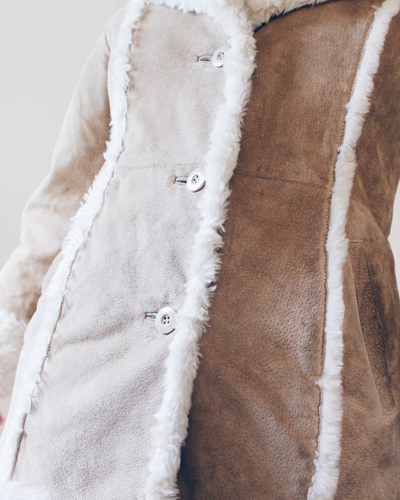 May include: A brown suede jacket with a white faux fur trim. The jacket has a button closure and a pocket on the right side.