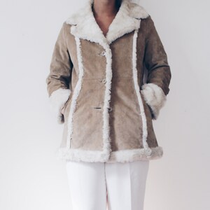May include: A brown suede jacket with a white faux fur collar and trim. The jacket has a button closure and is lined with white faux fur.