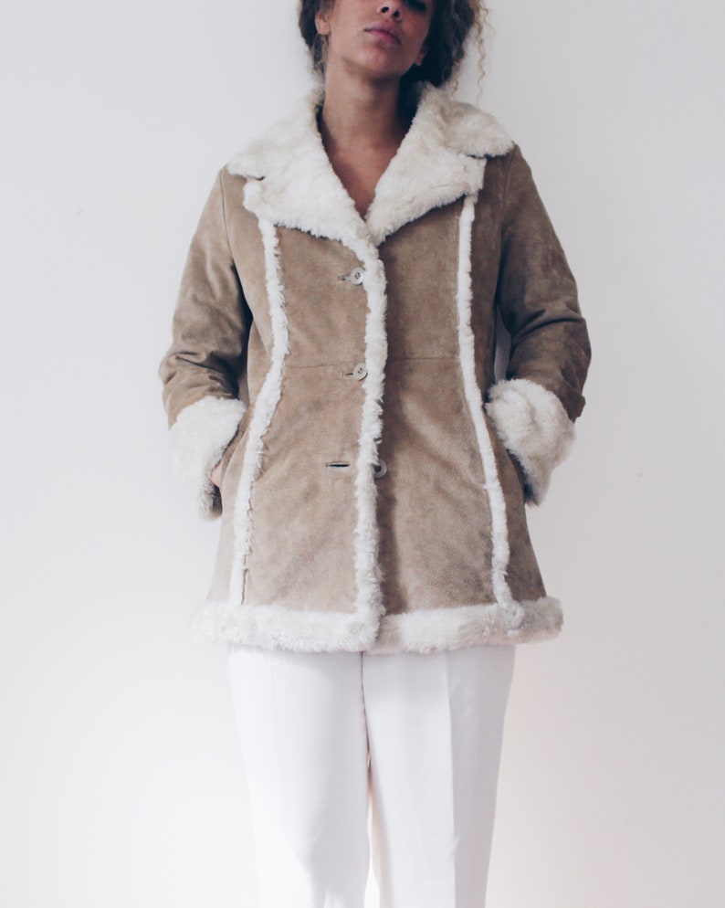 May include: A brown suede jacket with a white faux fur collar and trim. The jacket has a button closure and is lined with white faux fur.