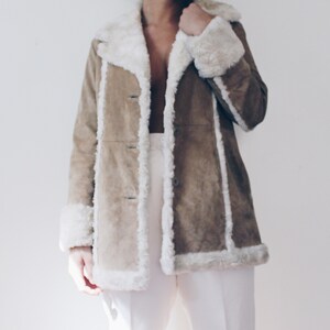 May include: A brown suede jacket with a white faux fur collar and trim. The jacket has a long, fitted silhouette and a button closure.