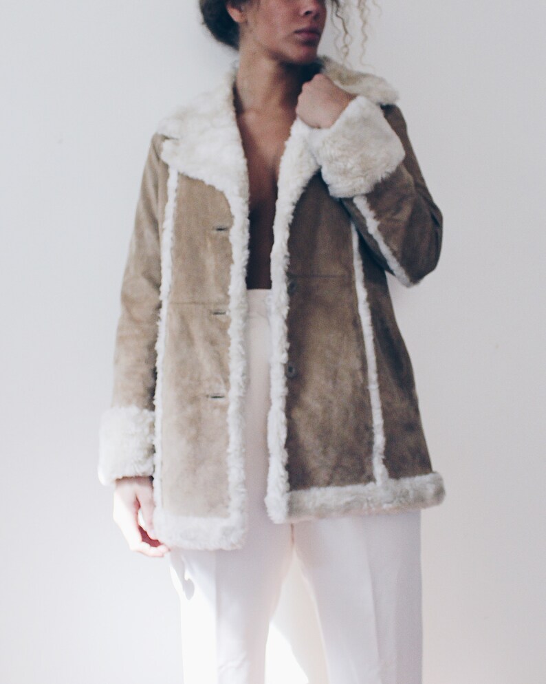 May include: A brown suede jacket with a white faux fur collar and trim. The jacket has a long, fitted silhouette and a button closure.