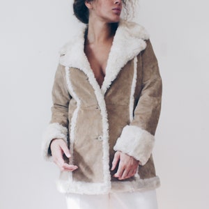 May include: A brown suede jacket with a white faux fur collar and cuffs. The jacket has a button closure and a long, fitted silhouette.
