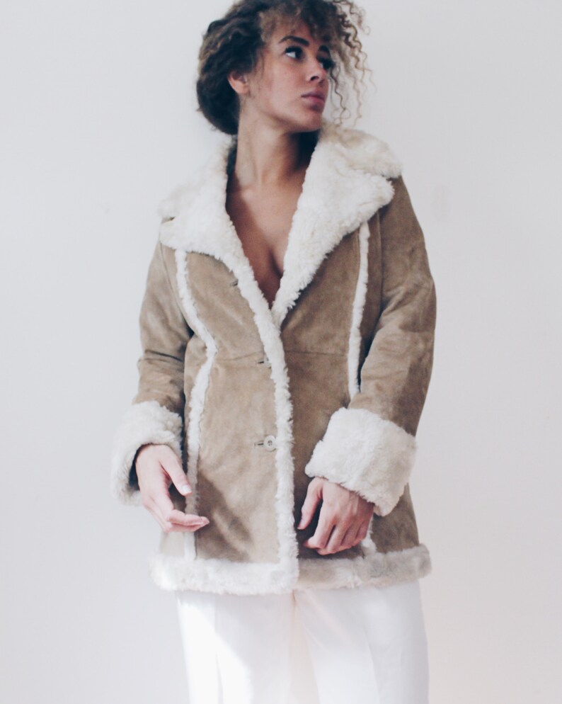 May include: A brown suede jacket with a white faux fur collar and cuffs. The jacket has a button closure and a long, fitted silhouette.