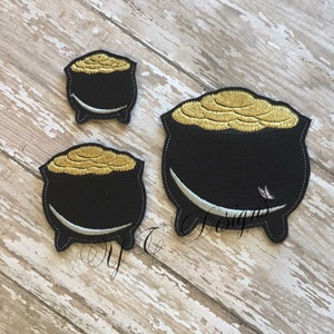 May include: Three black felt pot of gold patches with gold coin embroidery. The pots are different sizes.