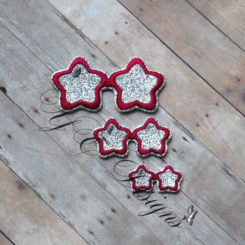 May include: Three pairs of star-shaped sunglasses with red frames and silver glitter lenses. The sunglasses are arranged in descending size on a wooden surface. The text "Designs" is visible in the lower left corner.