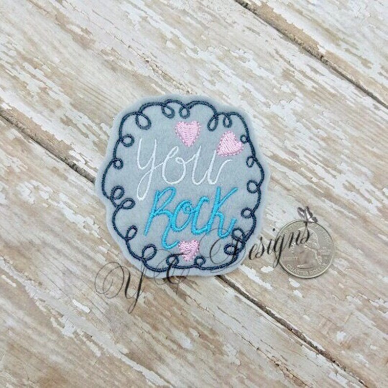 May include: Embroidered patch with a blue and white swirl border. The text "You Rock" is in white with blue accents. There are three pink hearts in the design.