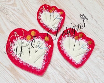 May include: Three red felt heart-shaped pincushions with white lace trim and gold accents. Each pincushion has a white felt center with multiple needles and thread.