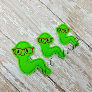 May include: Three green felt worm appliques with red glasses. Each worm has a smiling face and is curled into a C shape.