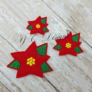 May include: Three felt poinsettia ornaments in red with green leaves and yellow centers. The ornaments are on a white wood background.