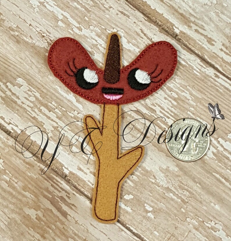 Op de afbeelding: Een vilt applique van een cartoon hotdog met een glimlachend gezicht en wimpers. De hotdog zit op een stok met een bruine vilt steel.