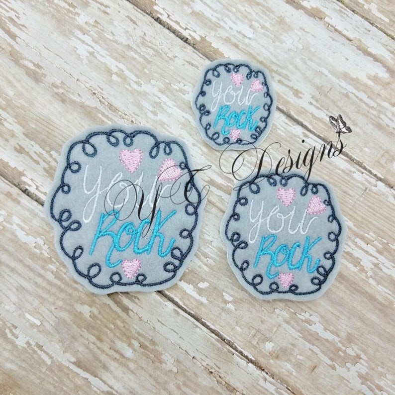May include: Three embroidered patches with a grey background and a black curly border. The patches say "You Rock" with pink hearts and blue text.